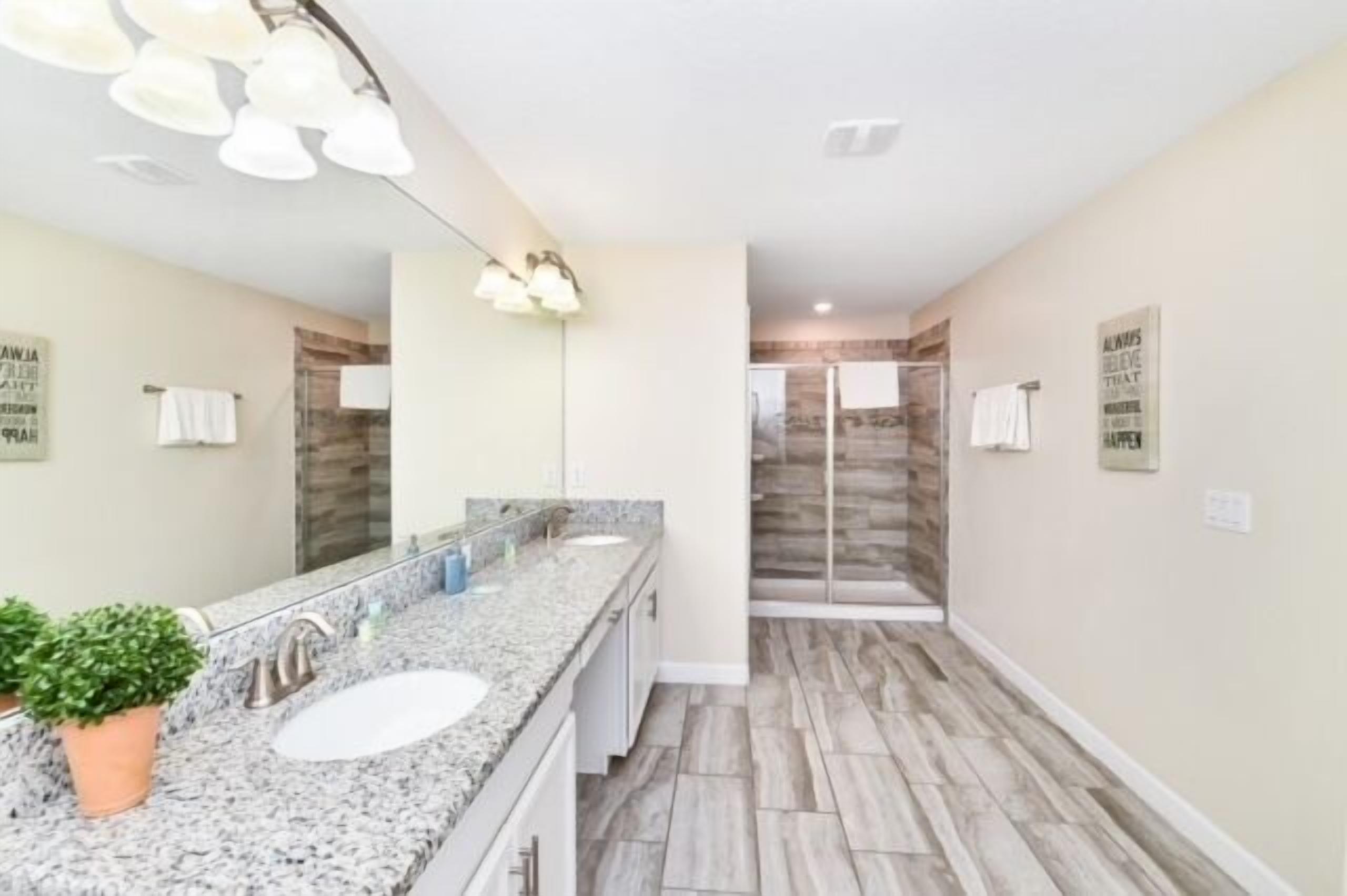 A modern bathroom with a granite countertop, two sinks, a large mirror, and a shower area with a glass door.