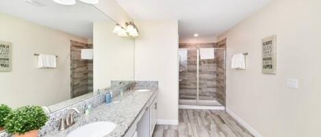 A modern bathroom with a granite countertop, two sinks, a large mirror, and a shower area with a glass door.