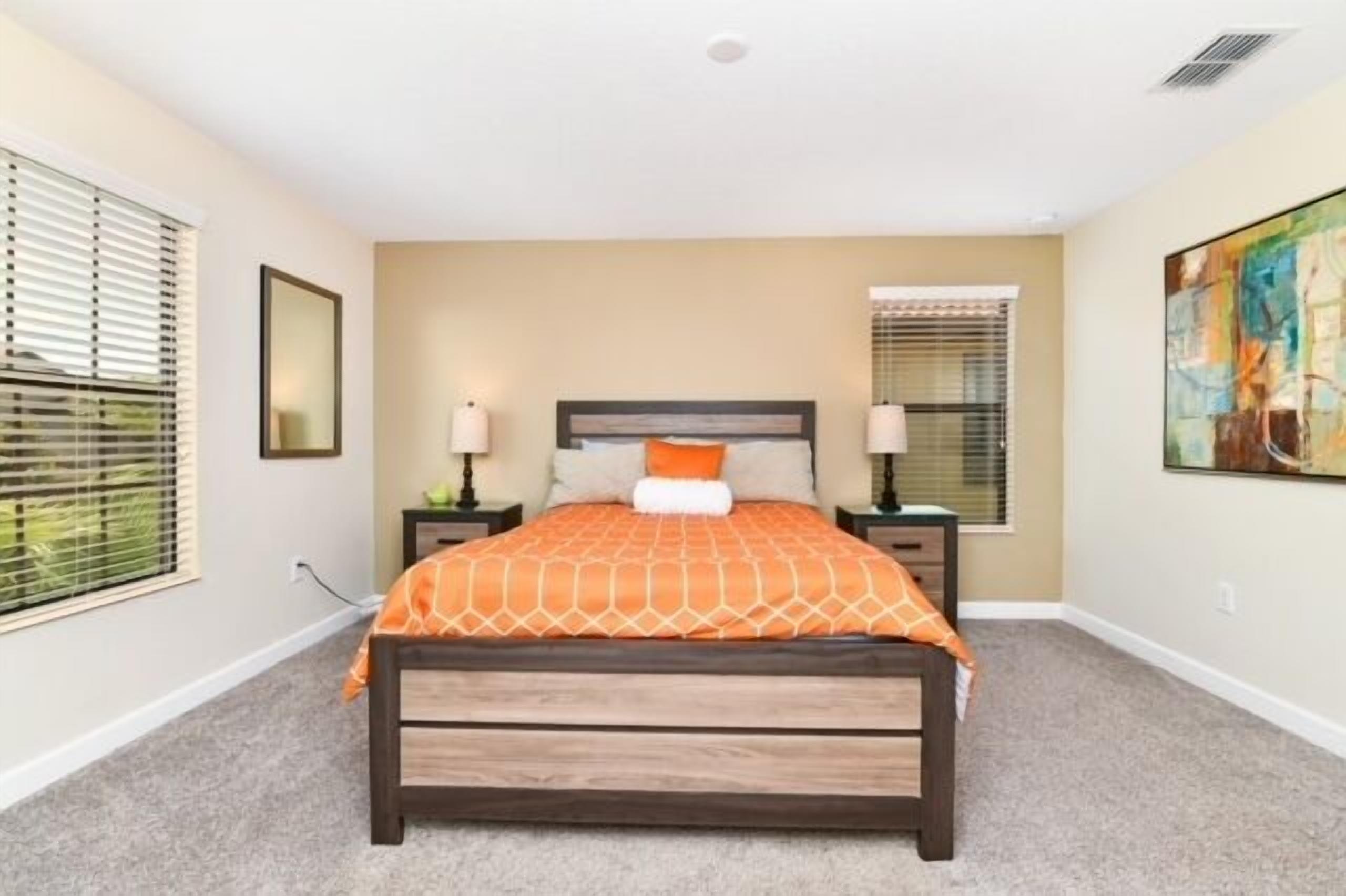 A bedroom with a bed, two nightstands, a window with blinds, and a painting on the wall.