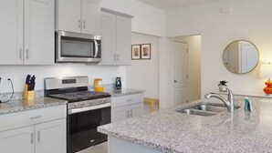 A modern kitchen with white cabinets, stainless steel appliances, granite countertops, and a large island with a sink. - Beautiful 5 Bed Pool Home with Game Room (Davenport)