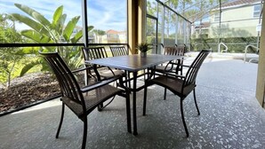 Une terrasse couverte avec une table et des chaises, de grandes fenêtres et une vue sur les environs.