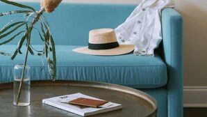 Una habitación con un sofá azul, una mesa redonda con un vaso de agua, un sombrero y un libro.