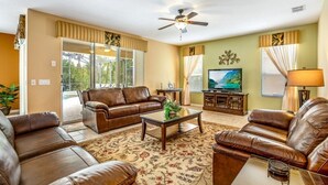A living room with leather sofas, a coffee table, a ceiling fan, and a television. - Spacious and Relaxing Home with South Facing Pool (Davenport)