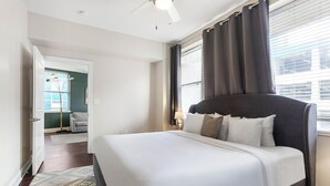A hotel room with a large bed, a ceiling fan, a window with curtains, and a view of the outside.