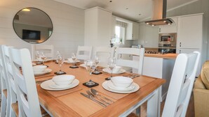 A dining area with a wooden table set for six, white chairs, and a round mirror on the wall. - 23 Meadow Retreat (Liskeard)