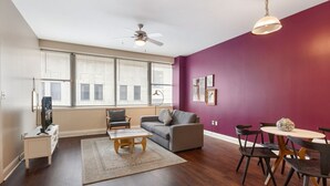 Un salon moderne avec un canapé gris, une table basse en bois, une table à manger avec des chaises et un ventilateur de plafond.