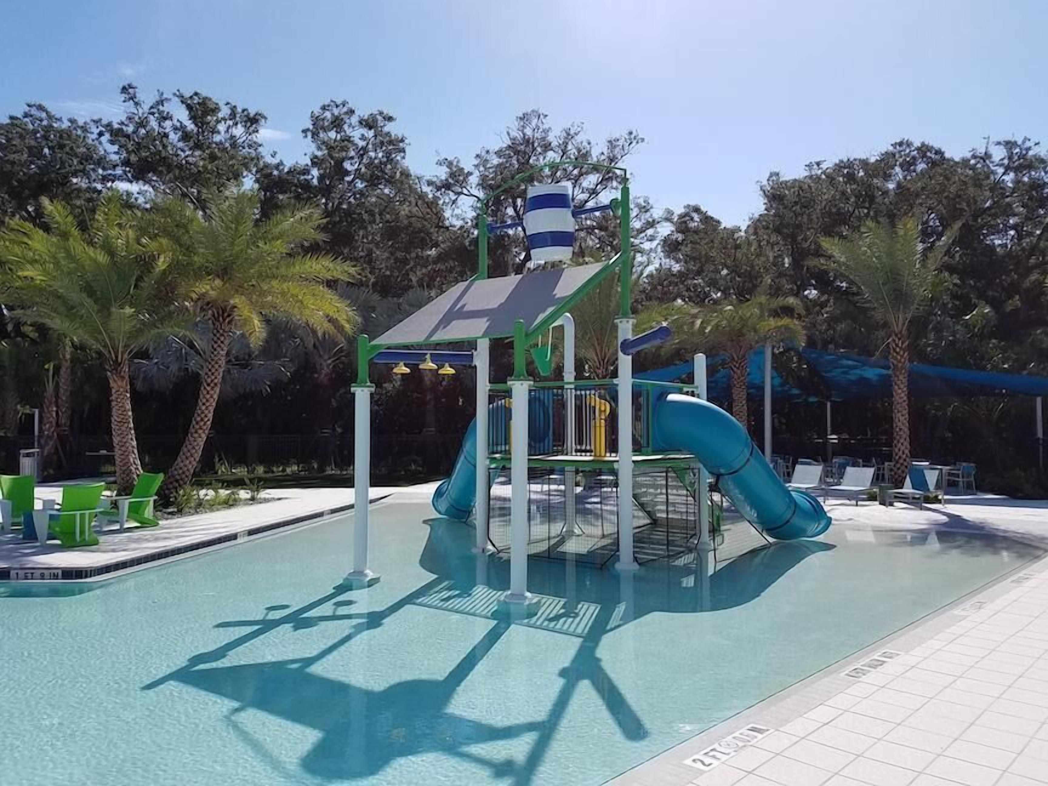 Ein Kinderspielbereich mit Rutsche und Klettergerüst, umgeben von einem Pool und Palmen.