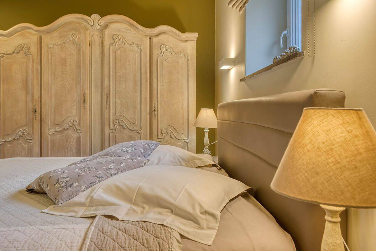 Un dormitorio con cabecera de madera, cama con ropa de cama color beige, lámpara de noche y un espejo instalado en la pared.