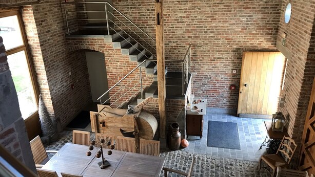 A spacious dining area with a high ceiling, exposed brick walls, and a central staircase. - B&B Hof ter Haegen (Galmaarden)