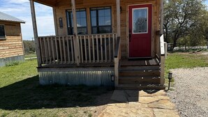 Une cabane en bois avec une porte rouge, un porche couvert et un chemin de pierres menant à l’entrée.