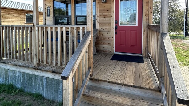 Une cabane en bois avec un porche couvert, une porte rouge et une petite fenêtre.