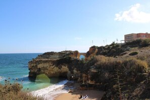A coastal landscape with a rocky cliff, a beach, and a building on the cliff.
