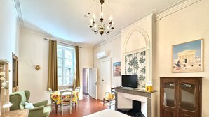 A hotel room with a large bed, a television, a fireplace, a dining area with a table and chairs, and a view of the outside. - Au Croco fleuri, 50m des arènes, terrasse (Nîmes)