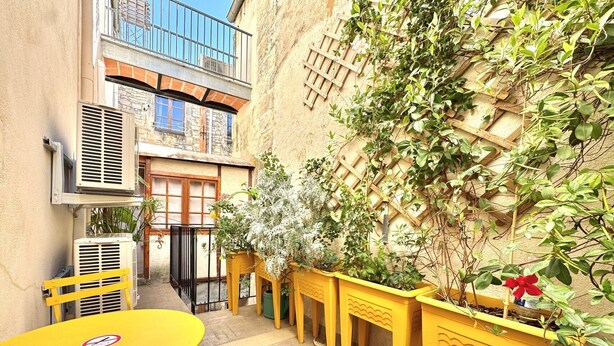 A courtyard with a yellow table and chairs, a wooden fence, and potted plants. - Au Croco fleuri, 50m des arènes, terrasse (Nîmes)