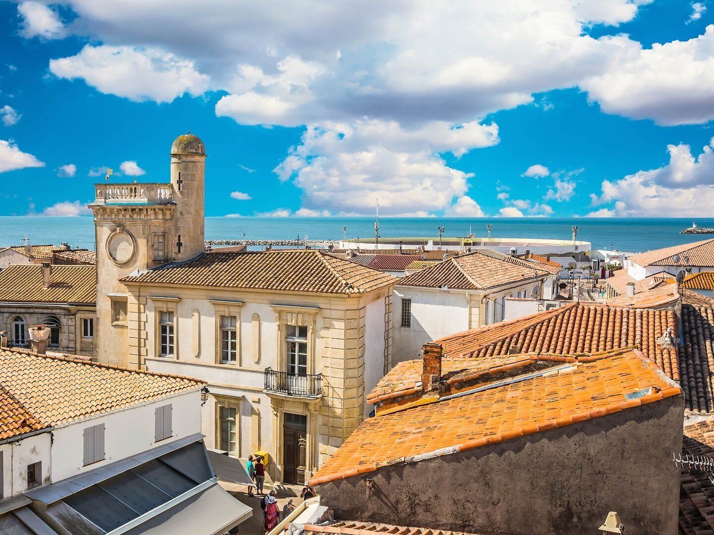 A coastal cityscape with historic buildings, a prominent tower, and a view of the sea.