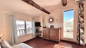 Une pièce avec un plafond en bois, un canapé, un téléviseur, un miroir en forme de soleil et une vue sur un jardin par la fenêtre.