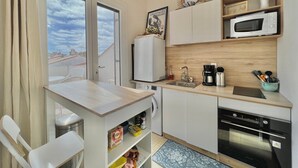 Une cuisine compacte équipée d’un four à micro-ondes, d’une machine à café et d’un four. Une fenêtre offre une vue sur la ville.