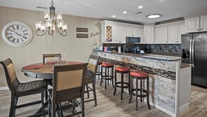 A kitchen with white cabinets, a stainless steel refrigerator, a dining table with chairs, and a bar area with stools. - Bridgepointe Condo 432 (Osage Beach)
