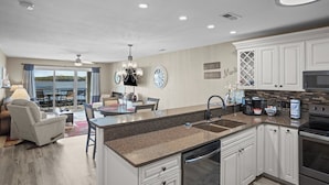 A modern kitchen with a central island, white cabinetry, and a dining area with a view. - Bridgepointe Condo 432 (Osage Beach)