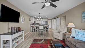 A living room with a TV, sofa, coffee table, and a ceiling fan. - Bridgepointe Condo 432 (Osage Beach)