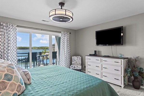 Un dormitorio con cama, cómoda, televisor y balcón con vista al agua.