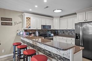 Una cocina moderna con armarios blancos, un refrigerador de acero inoxidable, una encimera de granito y taburetes rojos.