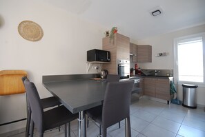 Una cocina moderna con encimera oscura, dos sillas, microondas, horno y un lavamanos.