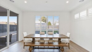 A dining room with a wooden table and white chairs, large windows with blinds, and a view of the outside. - Cowes Market Oasis with private pool (Cowes)