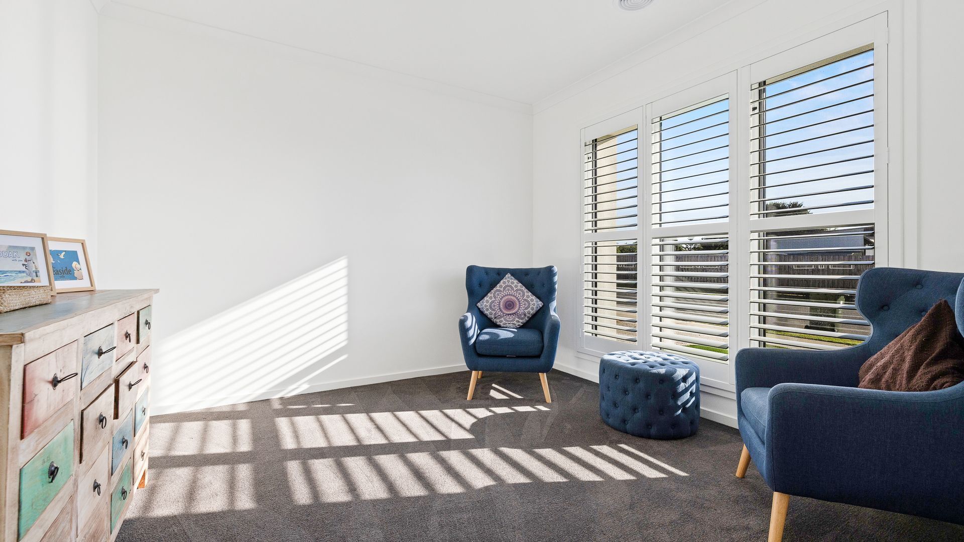 A room with a blue armchair, a matching ottoman, and a wooden dresser with multiple drawers.