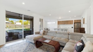 A modern living room with a sectional sofa, a coffee table, and a view of a backyard with a pool and patio furniture. - Cowes Market Oasis with private pool (Cowes)
