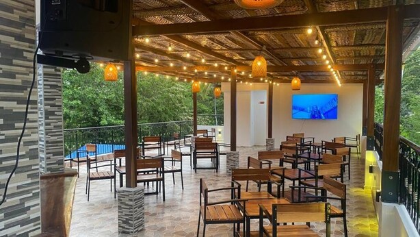 An outdoor seating area with stone flooring, wooden tables and chairs, and string lights.