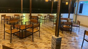 An outdoor seating area with wooden tables and chairs, stone flooring, and hanging lights.