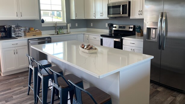 A modern kitchen with white cabinetry, a large island with bar stools, stainless steel appliances, and a window providing natural light. - Unwind and relax at this luxurious mountain retreat. Beautiful Views! (Sparta)
