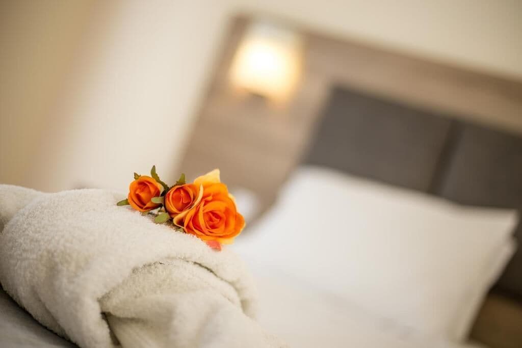 A neatly made bed with a white blanket and two orange roses.