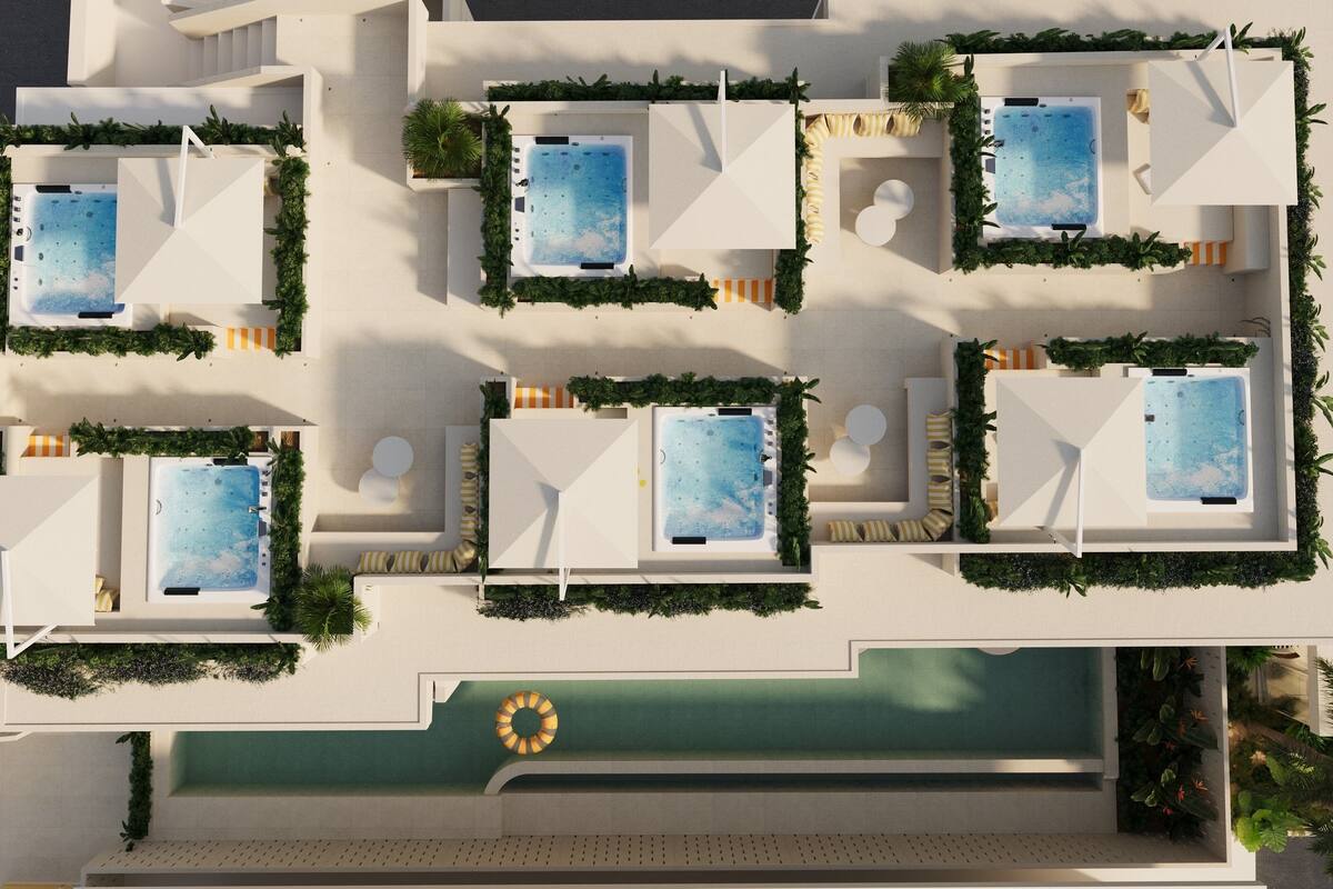 A rooftop pool area with multiple hot tubs and lounge chairs, surrounded by greenery.