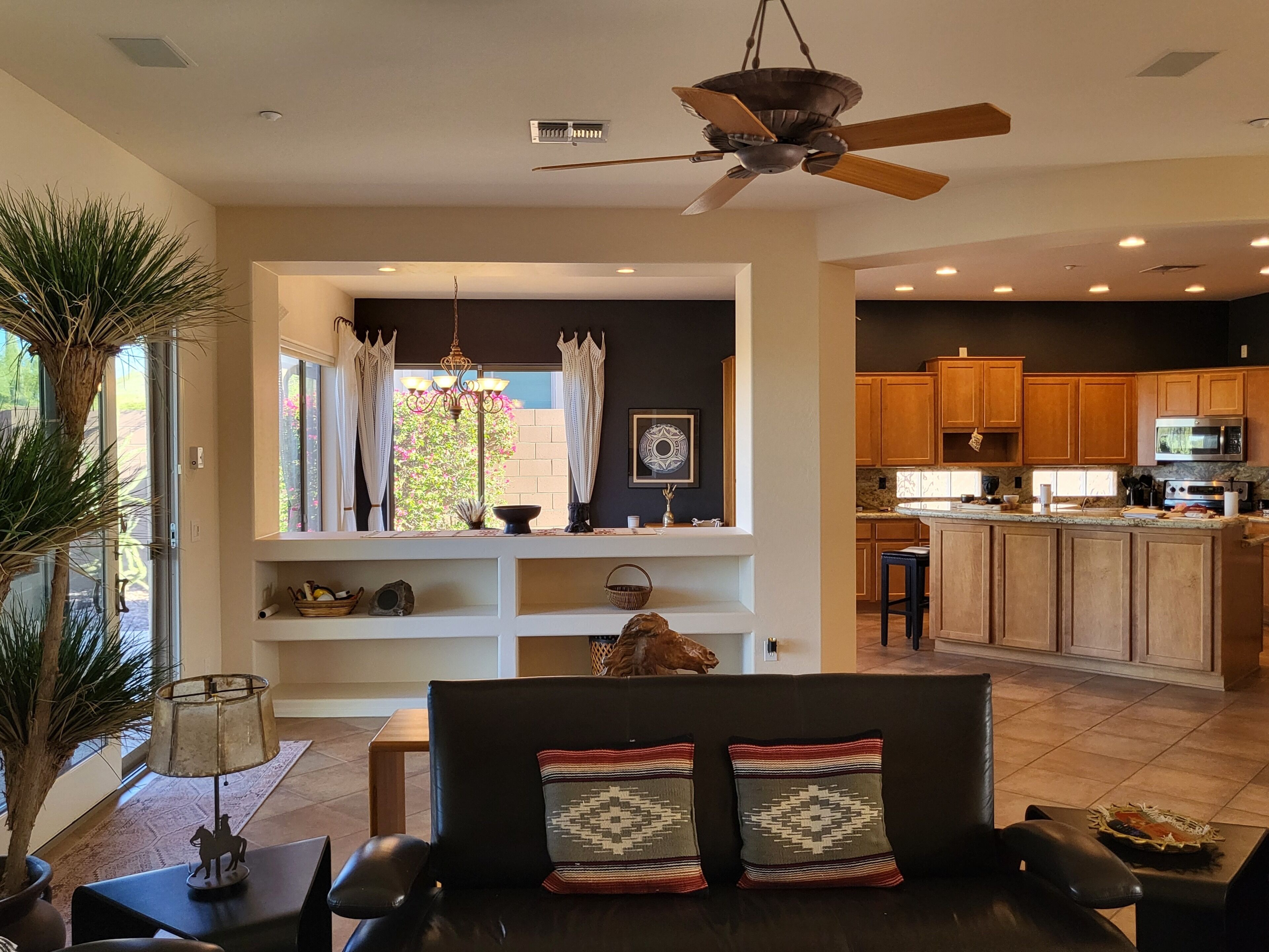 A modern living room with a sofa, a dining table, a ceiling fan, and a view of the kitchen.
