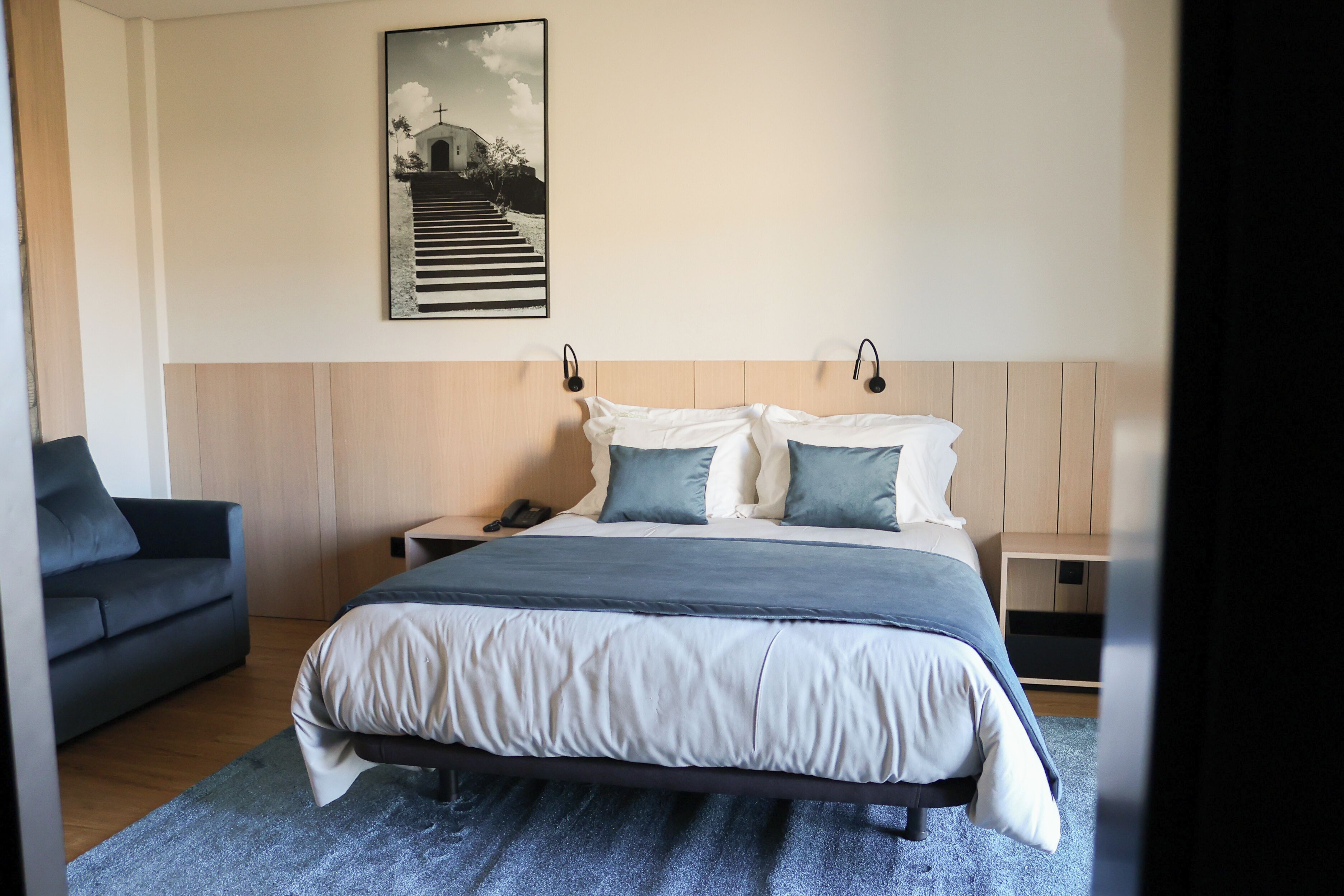 Un dormitorio con cama, mesita de noche, sofá y un cuadro en la pared.