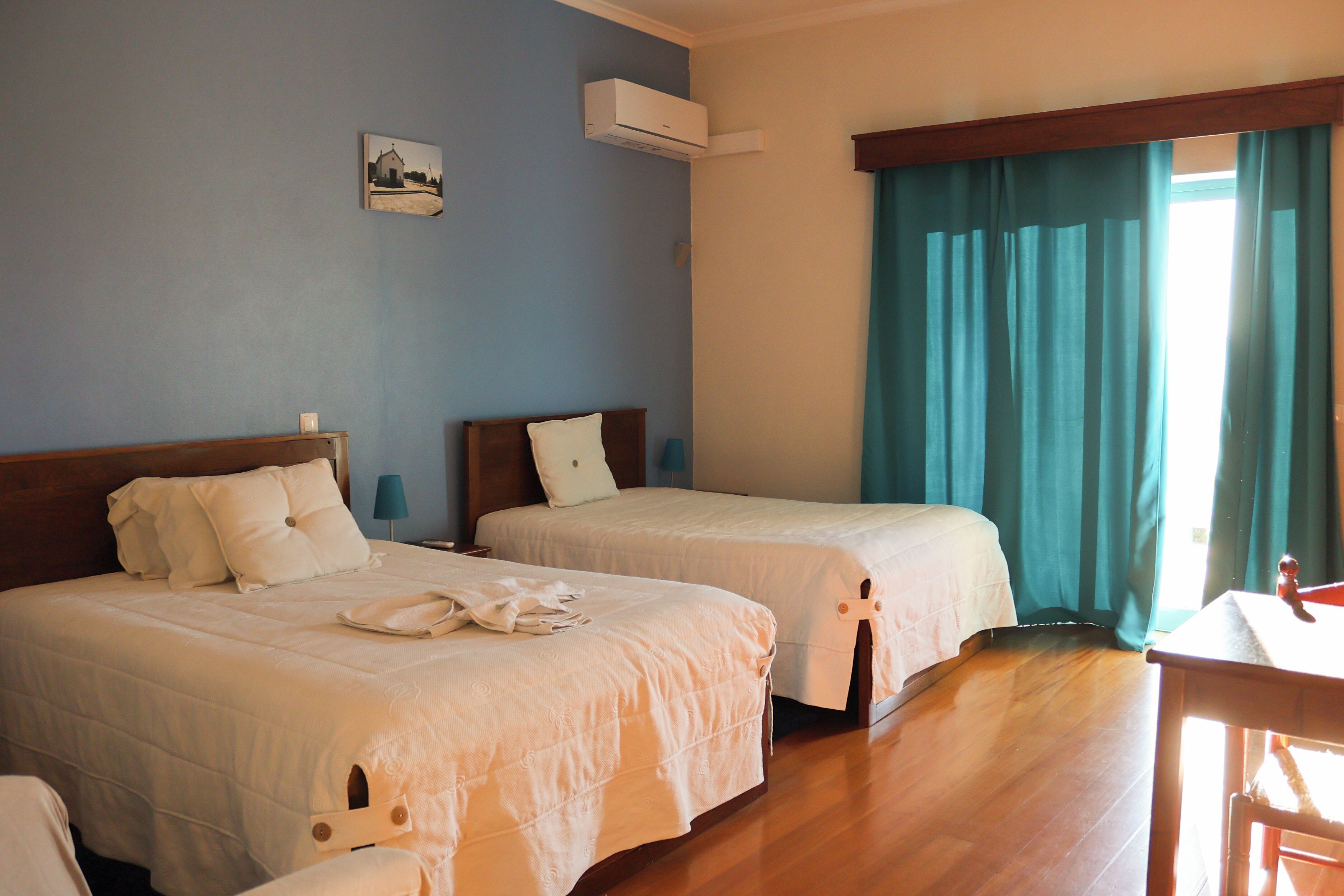 Habitación de hotel con dos camas, cabecero de madera, una mesita pequeña y una ventana con cortinas.