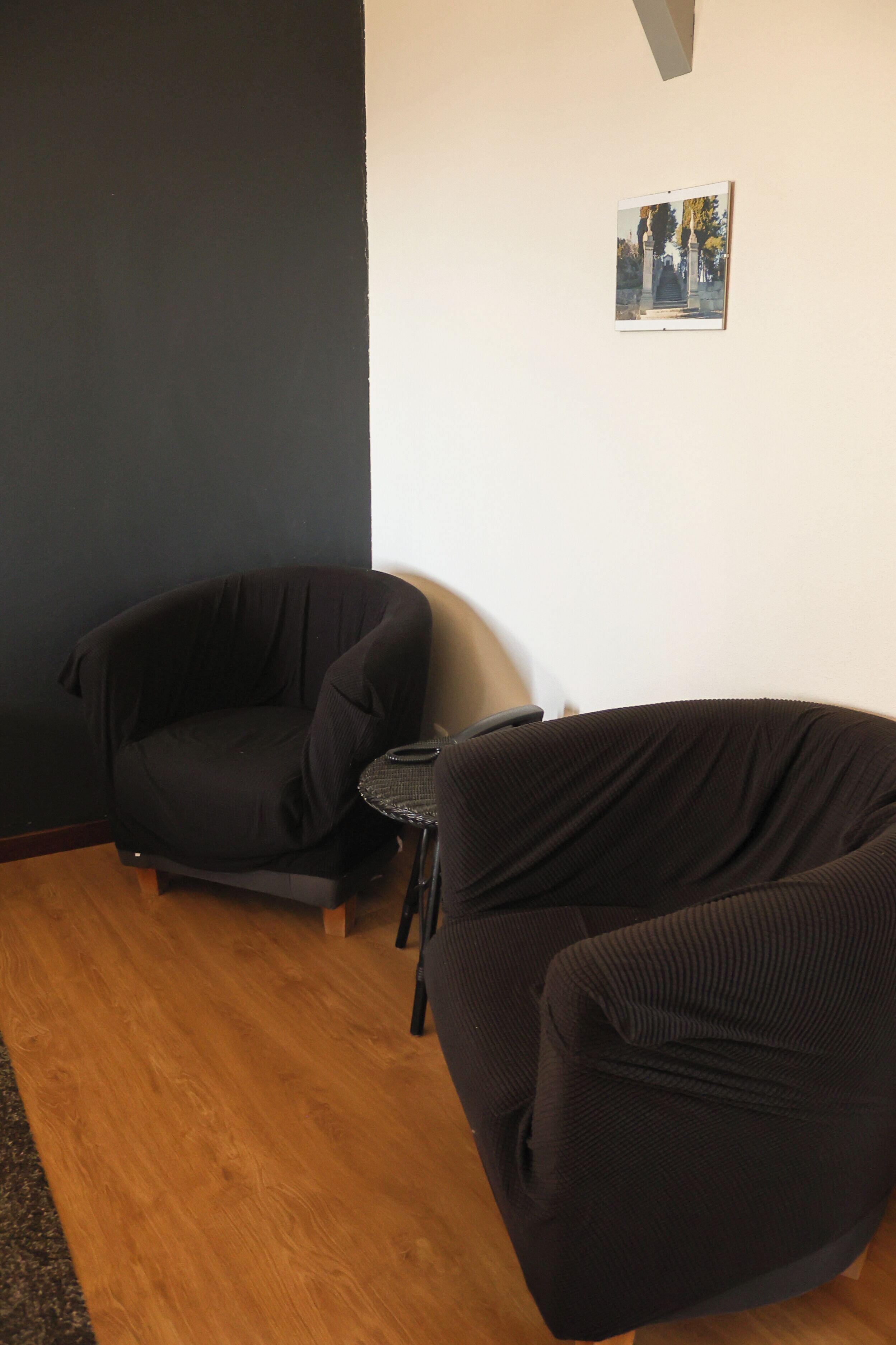 A room with two black sofas, a small table, and a framed picture on the wall.