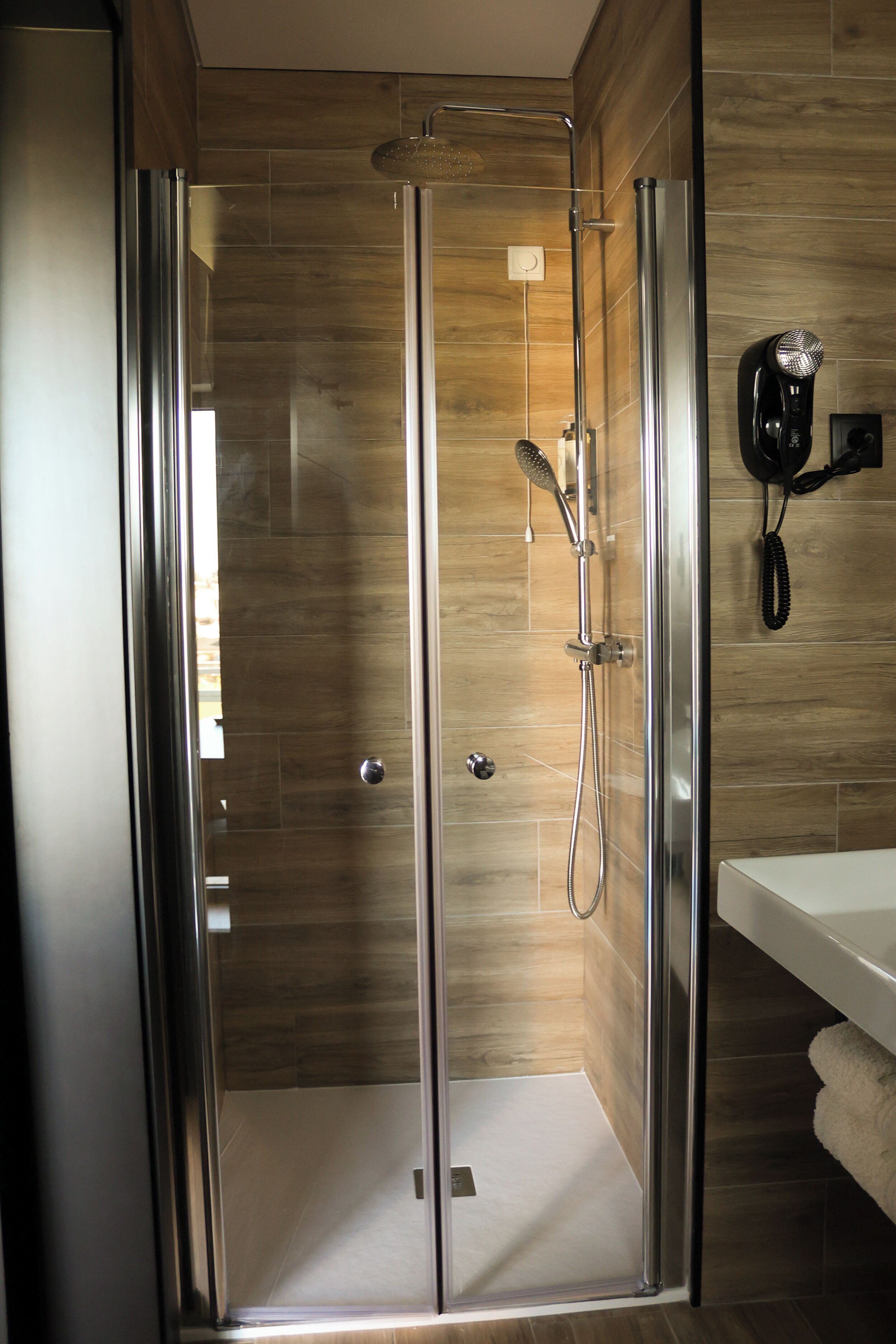 A modern bathroom with a glass-enclosed shower, a white sink, and a towel rack.