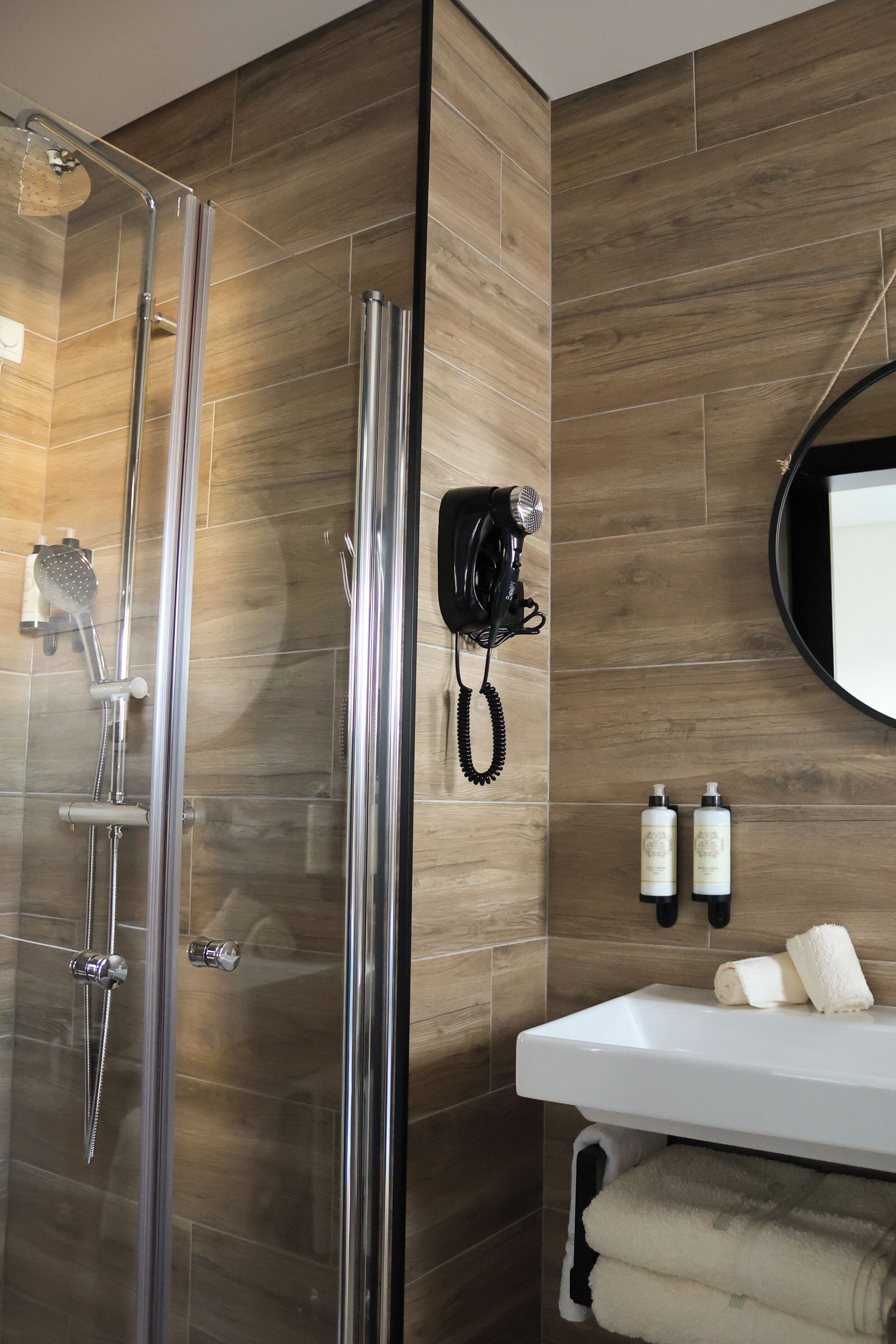 Ein modernes Badezimmer mit einer Duschkabine aus Glas, einem weißen Waschbecken und zwei Shampoo-Flaschen.