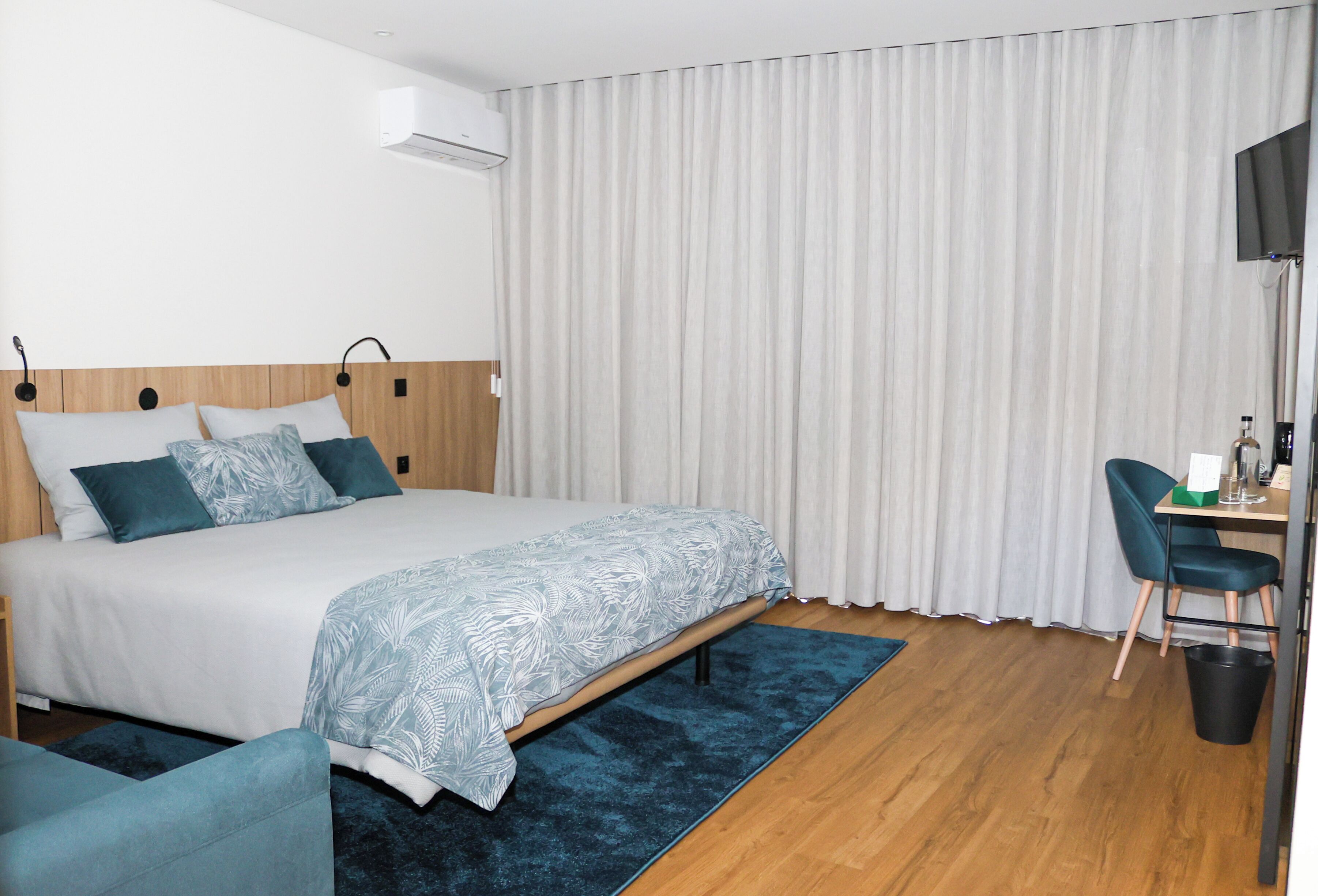 A hotel room with a bed, a desk, a chair, a TV, and a window with curtains.