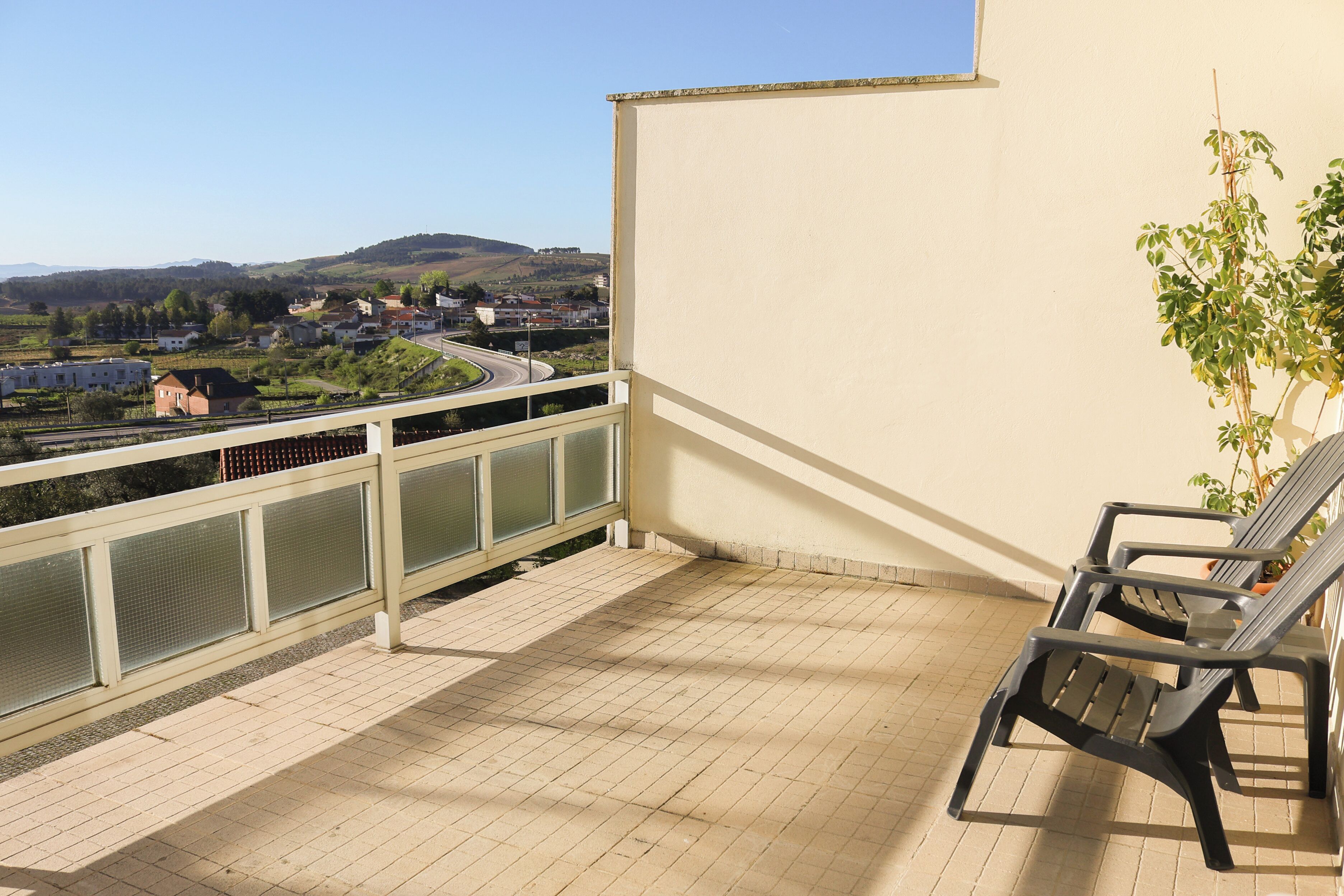 Varanda com vista para uma cidade e colinas, com grade e duas cadeiras.