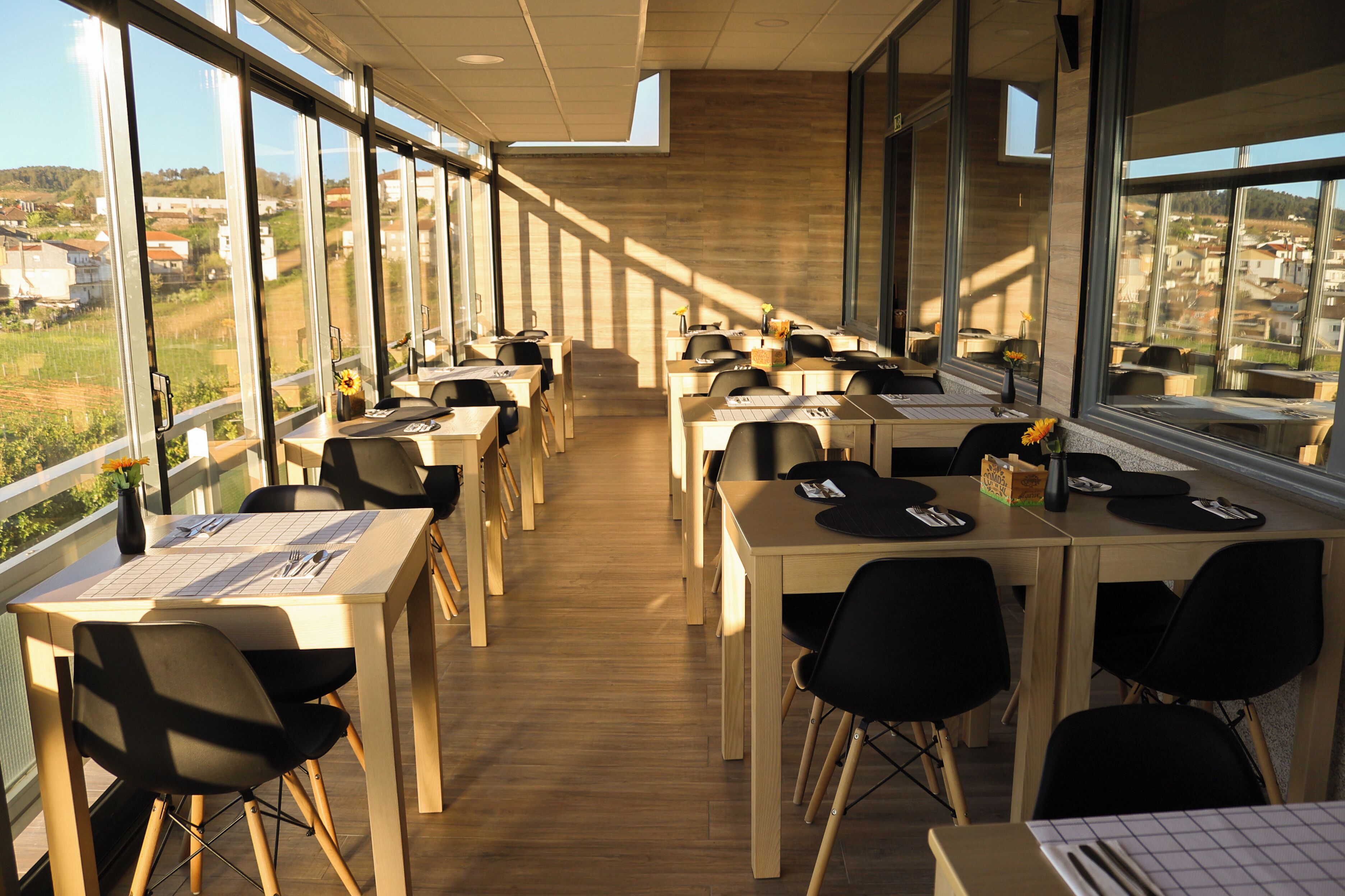 A modern dining area with long tables and chairs, large windows offering views of the surrounding landscape.