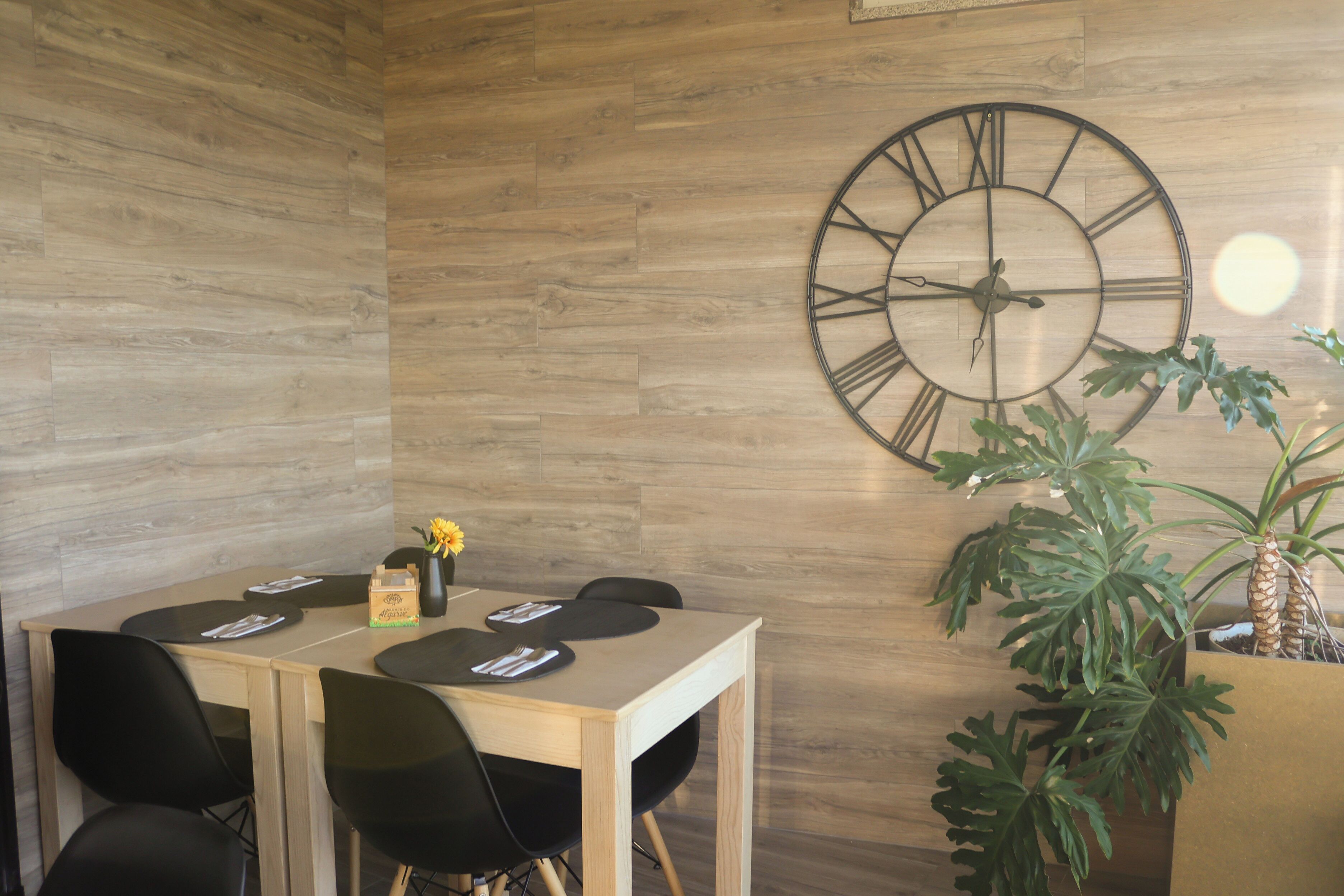Un comedor con una mesa de madera, sillas negras, un reloj de pared grande y una planta en maceta.