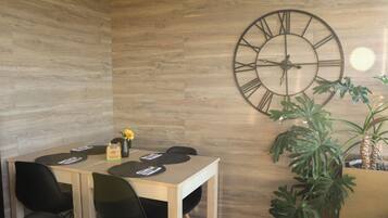Un comedor con una mesa de madera, sillas negras, un reloj de pared grande y una planta en maceta.