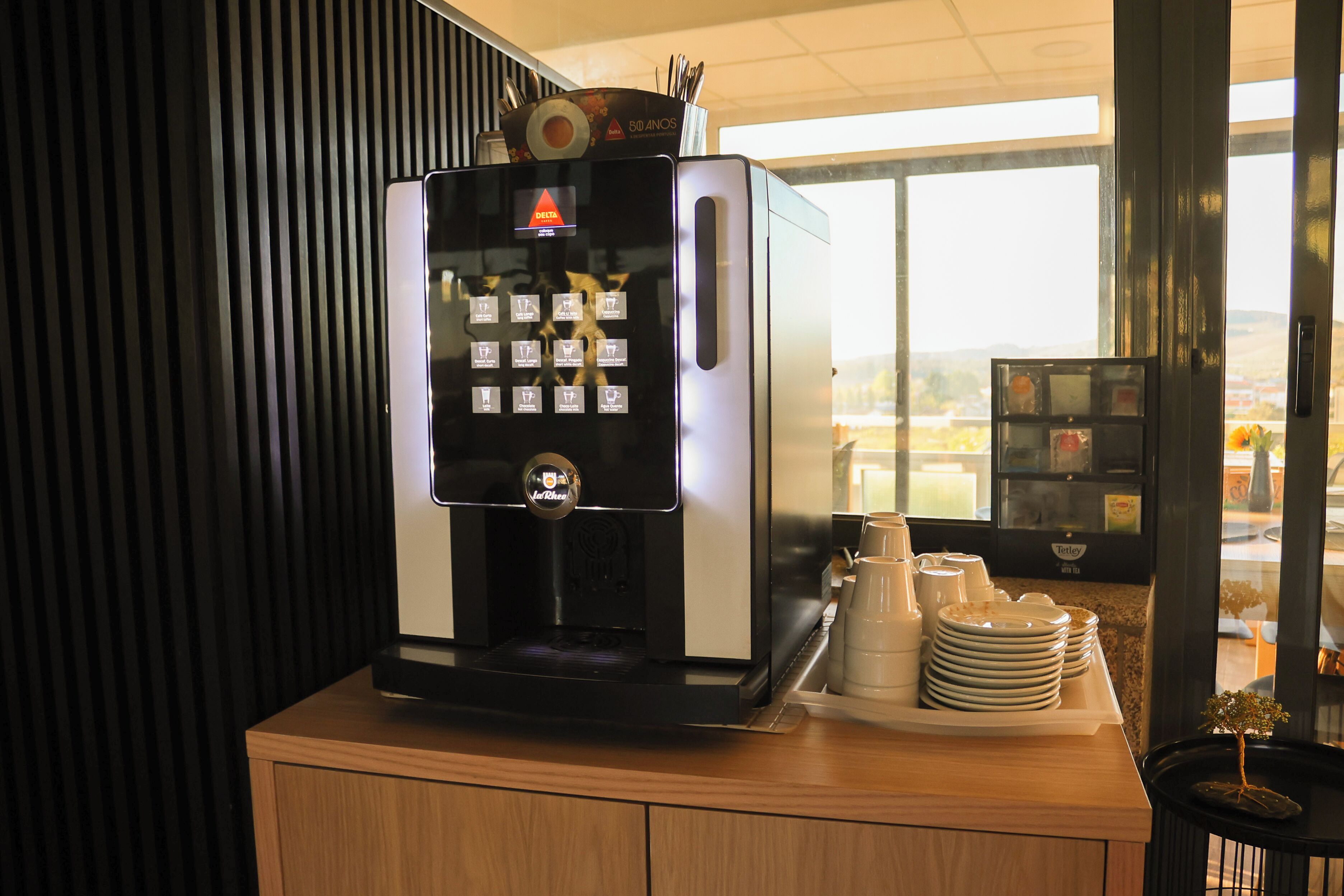 A coffee machine with a digital display, a tray of stacked plates, and a small potted plant on a counter.
