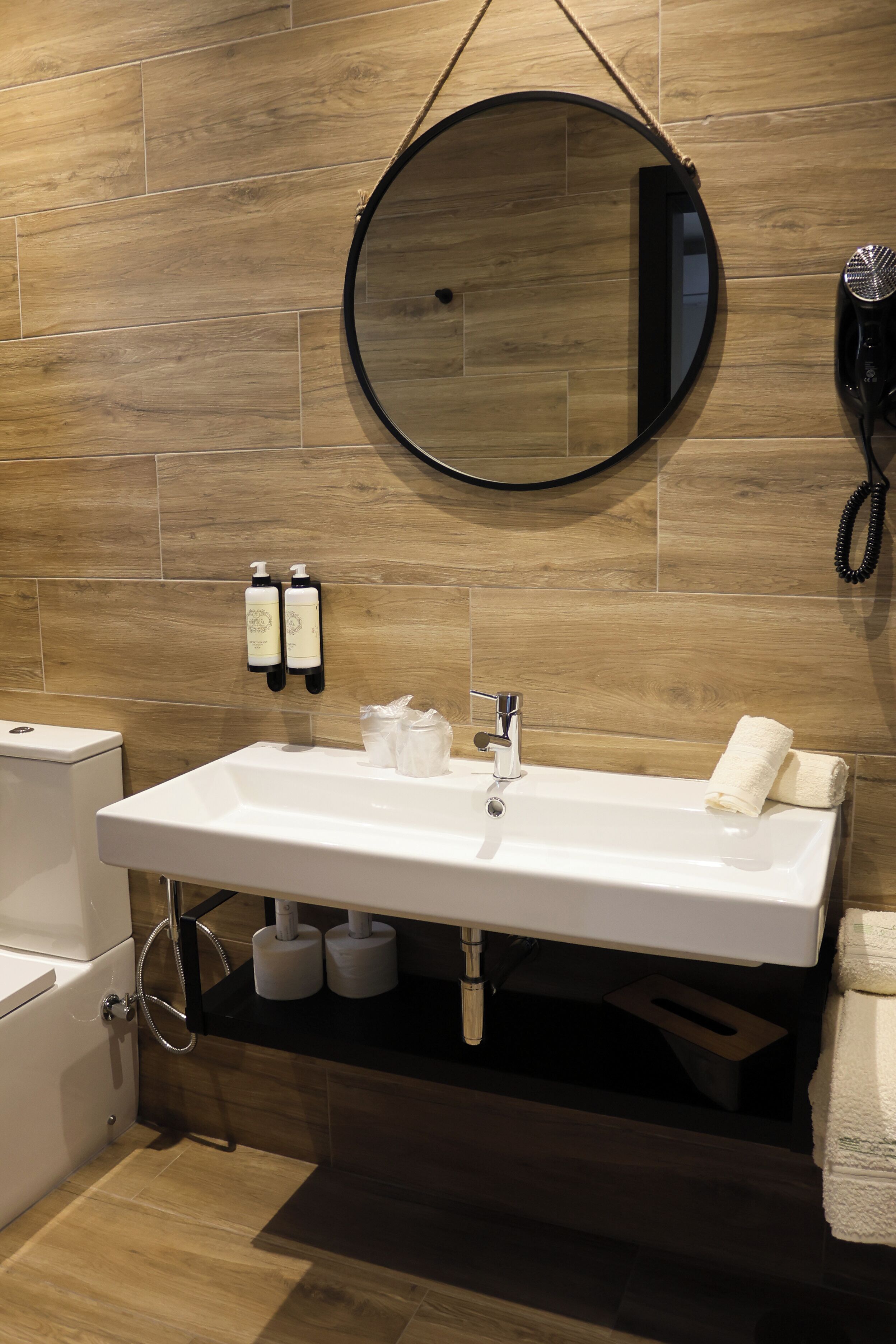 A bathroom with a white sink, mirror, and towel rack. There are two bottles of shampoo and a hairdryer on the wall.