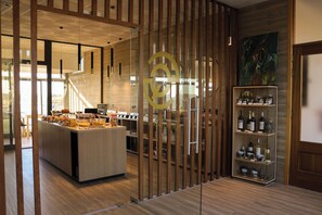 En moderne hotellobby med en central ø-disk, en glasafskærmning med et logo og et vinskab.
