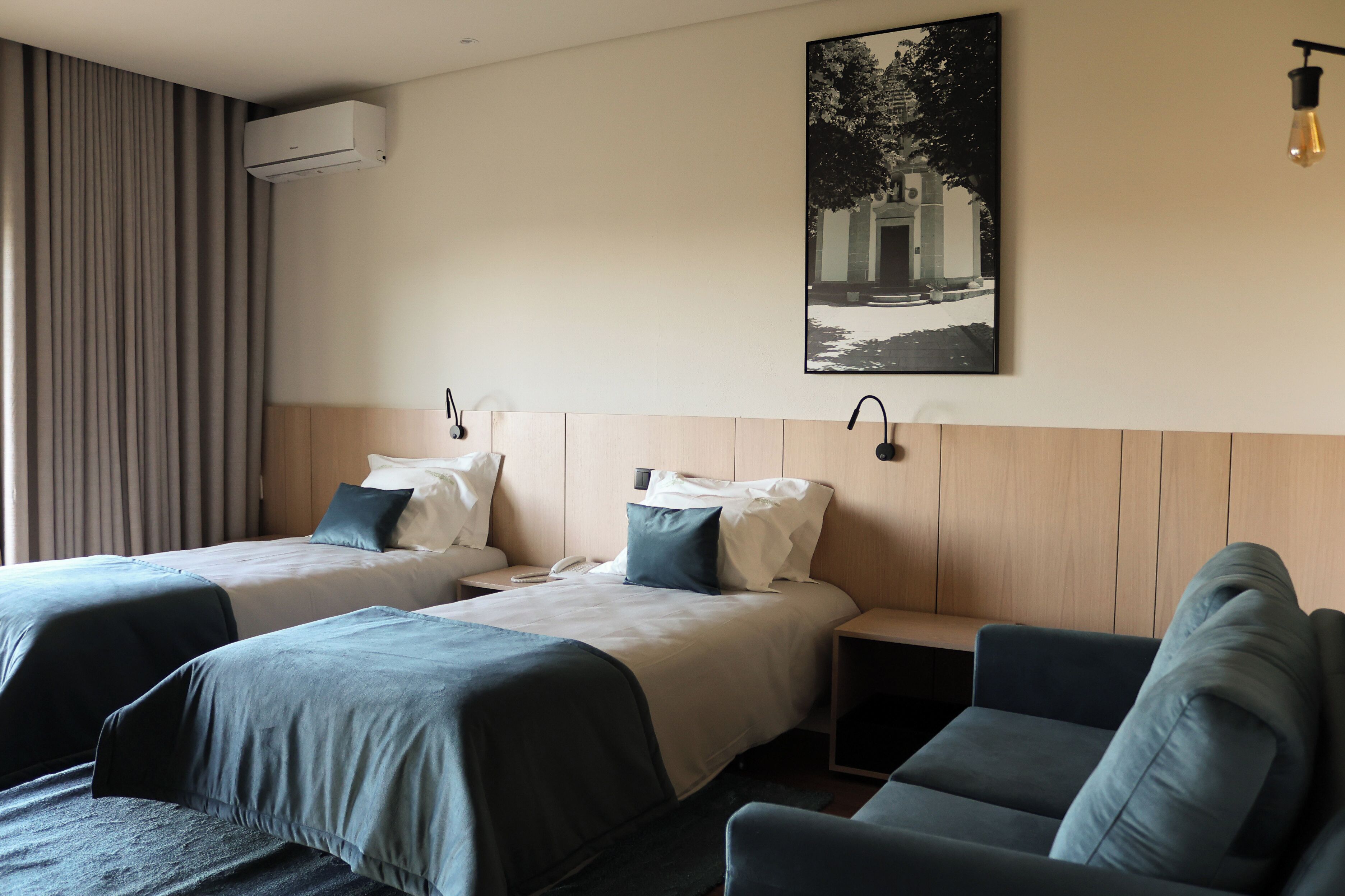 Quarto de hotel com duas camas, um sofá, uma escrivaninha, ar condicionado e um quadro pendurado na parede.